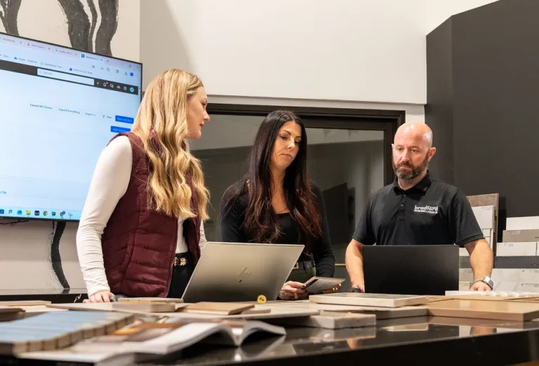 Three construction professionals reviewing project estimates on laptops in a design showroom.