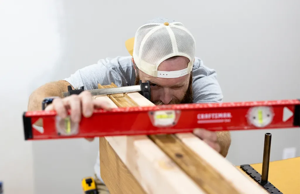 Man using a spirit level to check the alignment of clamped wooden boards